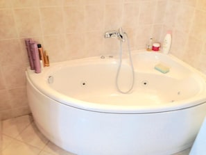 A white bathtub with a handheld showerhead, a bottle of shampoo, and a bar of soap.