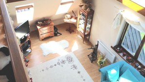 Ein gemütliches Zimmer mit Holzboden, einem weißen Teppich, einem blauen Sofa, einem Holzschrank und einem Fenster mit Blick ins Freie.