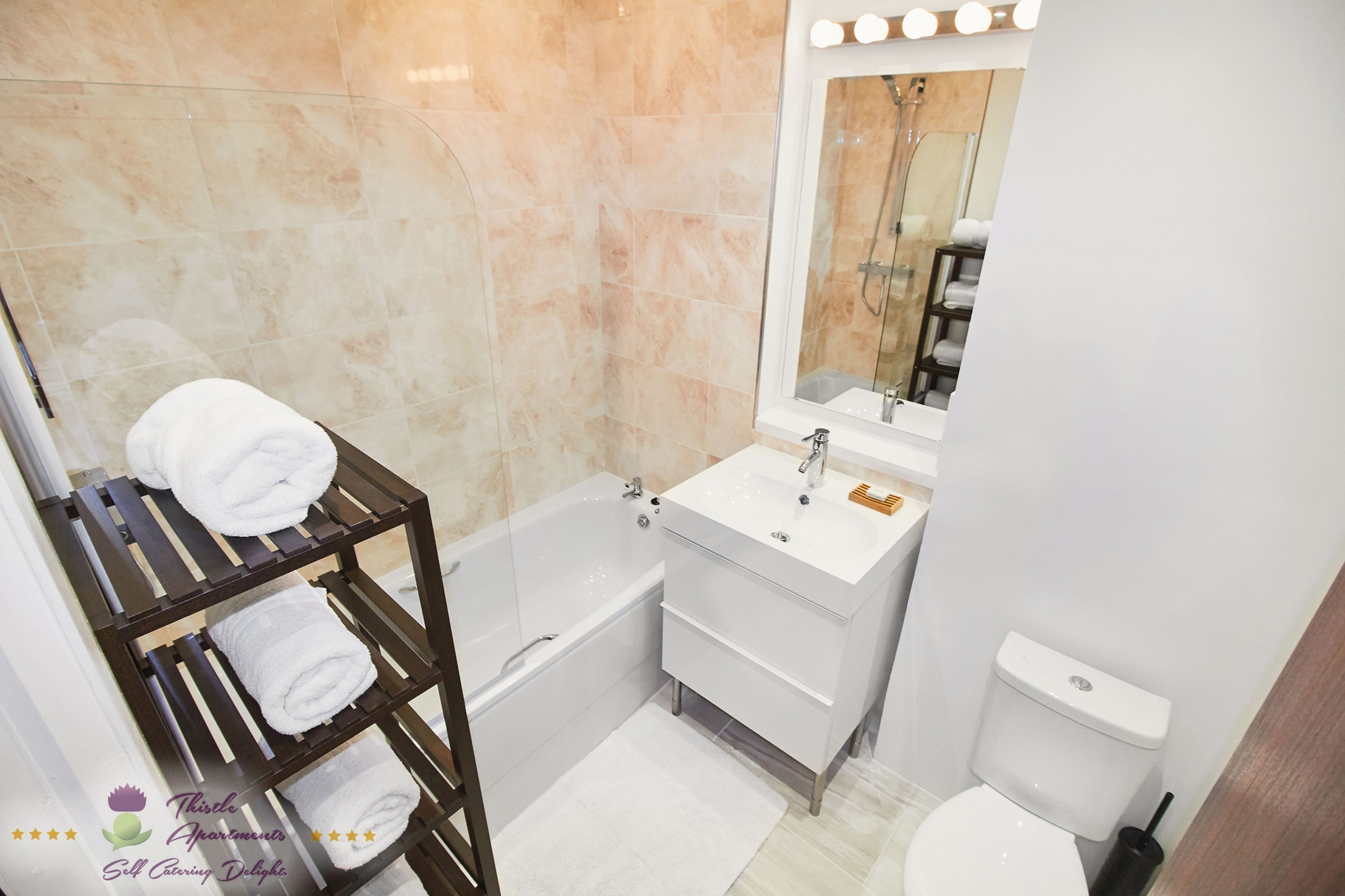 Un baño con bañera, un lavamanos blanco, un espejo y un perchero para toallas.