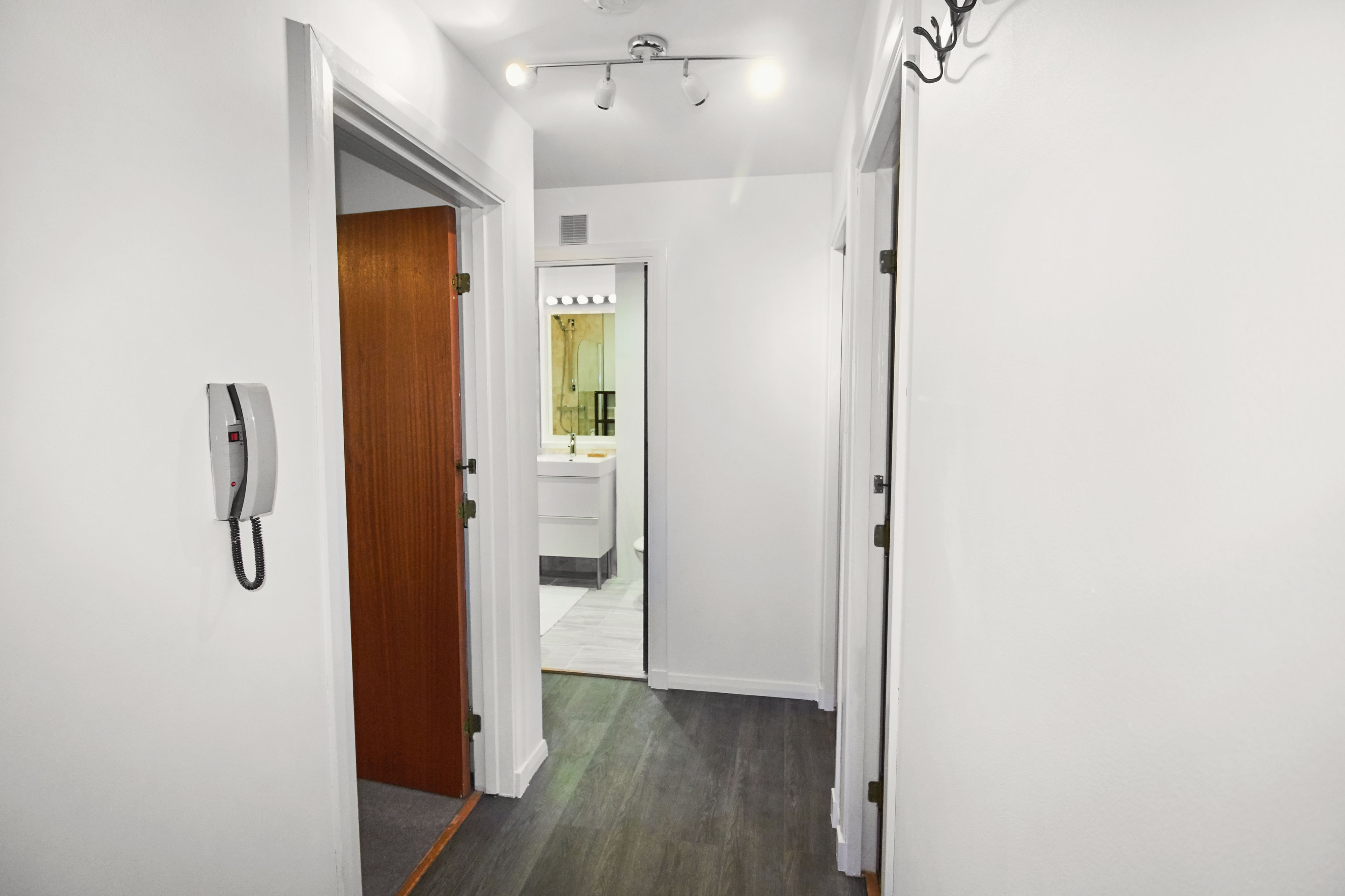A hallway with a telephone, a wooden door, and a bathroom visible in the distance.