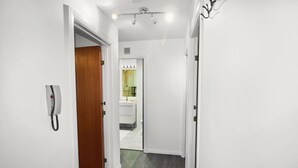 Un corridoio con un telefono, una porta in legno e un bagno visibile in fondo.