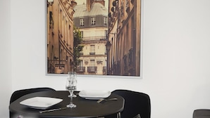 Angolo ristoro con tavolo apparecchiato per due, un quadro che raffigura una veduta cittadina e una segnaletica che indica 'Thirteenth Apartments Self Catering Delights'.