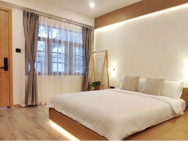 Un dormitorio moderno con una cama grande, piso de madera y una ventana con cortinas translúcidas.