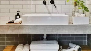 Un baño con un lavabo blanco, un espejo redondo, una planta y toallas sobre el mostrador.