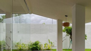 A modern outdoor patio with glass walls, wooden flooring, and a grassy area with plants. - Hotel AONO (Chiang Mai)