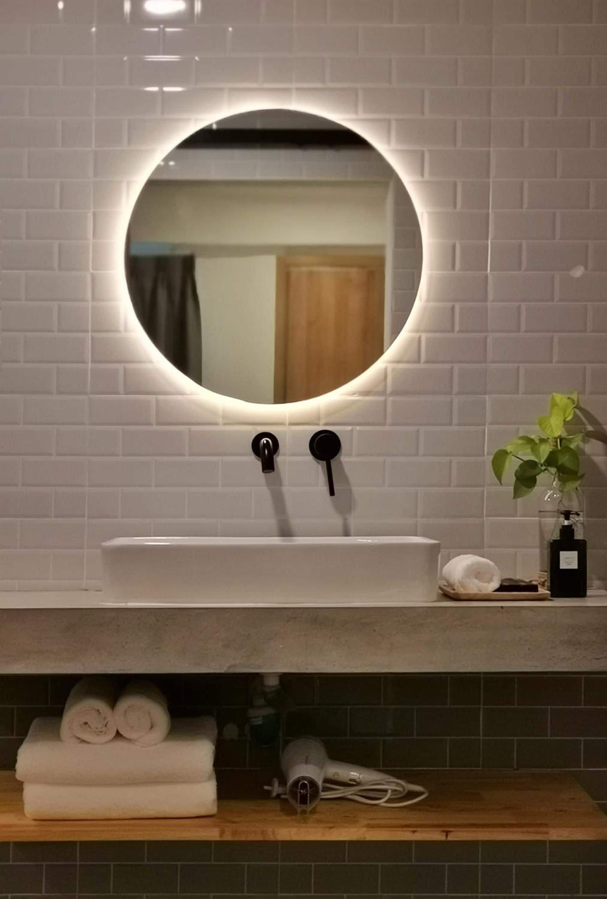 A bathroom with a white sink, a round mirror with a light, and a plant on the counter.