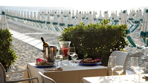 A table set for dining with a view of the beach and umbrellas in the background. - Miramare Resort (Pisa)