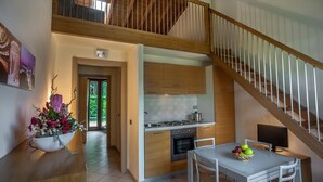 A modern kitchen with wooden cabinets, a dining table with chairs, and a staircase with a wooden railing. - Miramare Resort (Pisa)