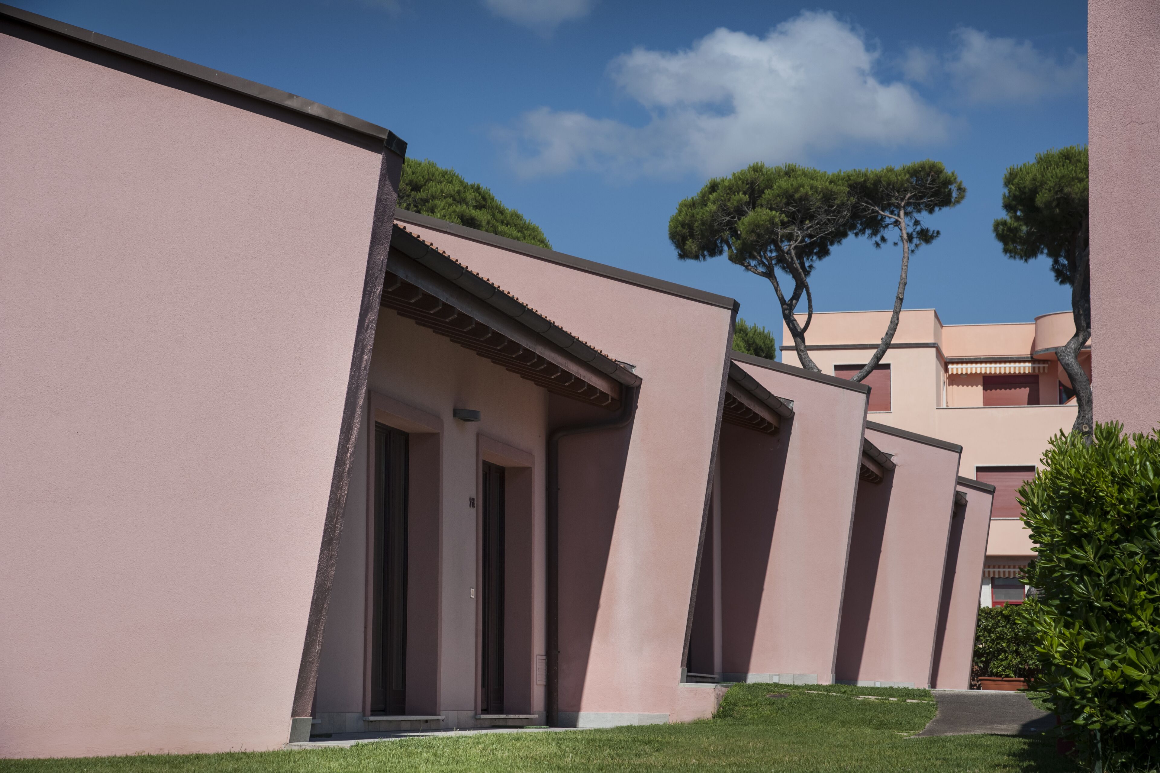 Una hilera de edificios rosados, cielo despejado y árboles al fondo.