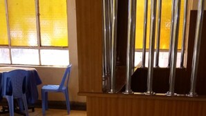 A room with a window, a blue plastic chair, a table, and a wooden partition with metal bars. - Chariot County Hotel (Machakos)