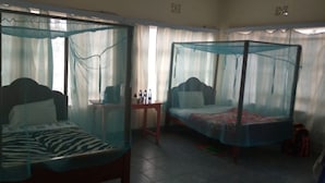 Two single beds with mosquito netting, a small table, and a chair in a room with curtains. - Chariot County Hotel (Machakos)