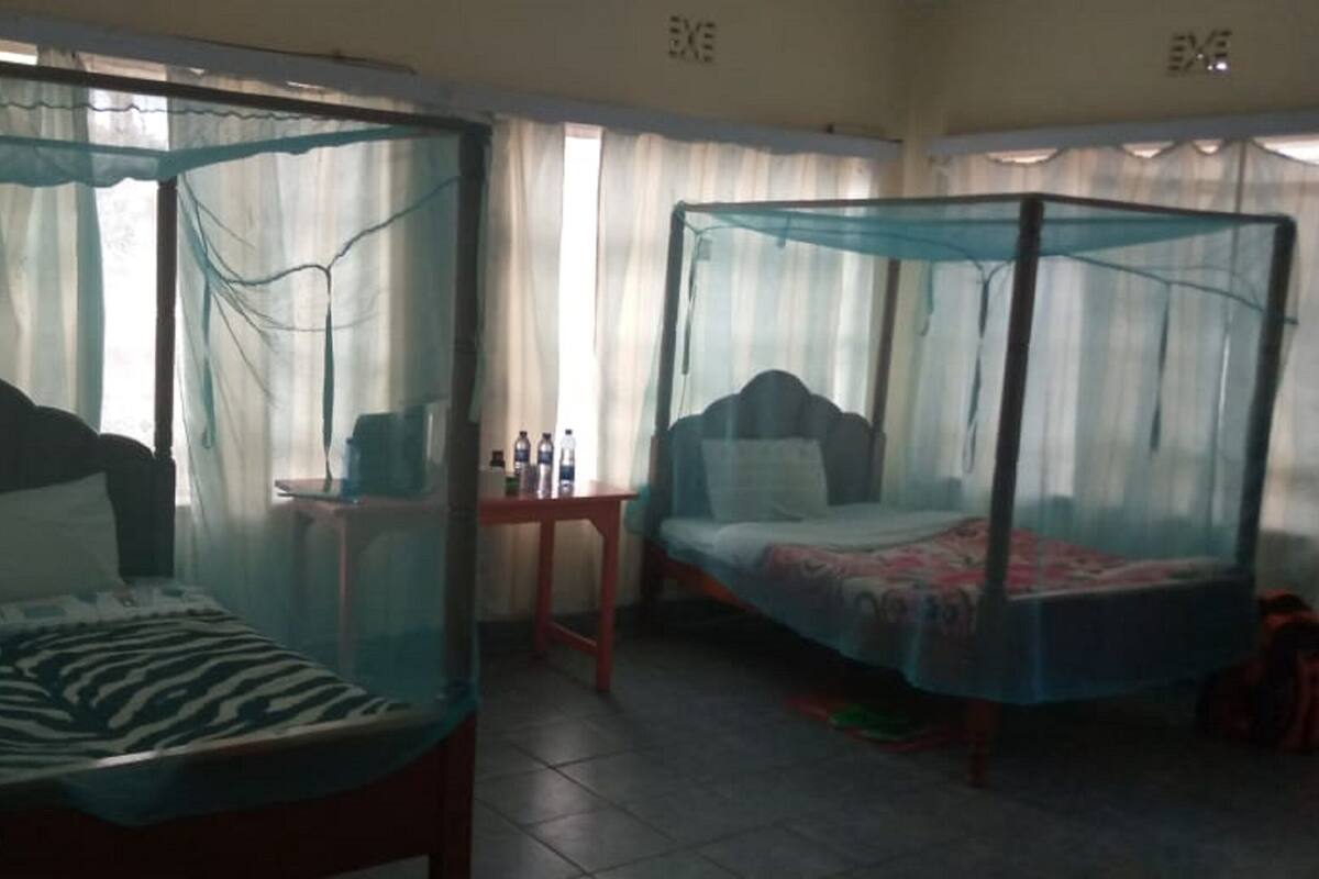 Two single beds with mosquito netting, a small table, and a chair in a room with curtains.