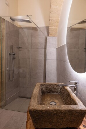 A modern bathroom with a glass-enclosed shower, a stone sink, and a large mirror. - L' Artiere Dimore nei Sassi (Matera)