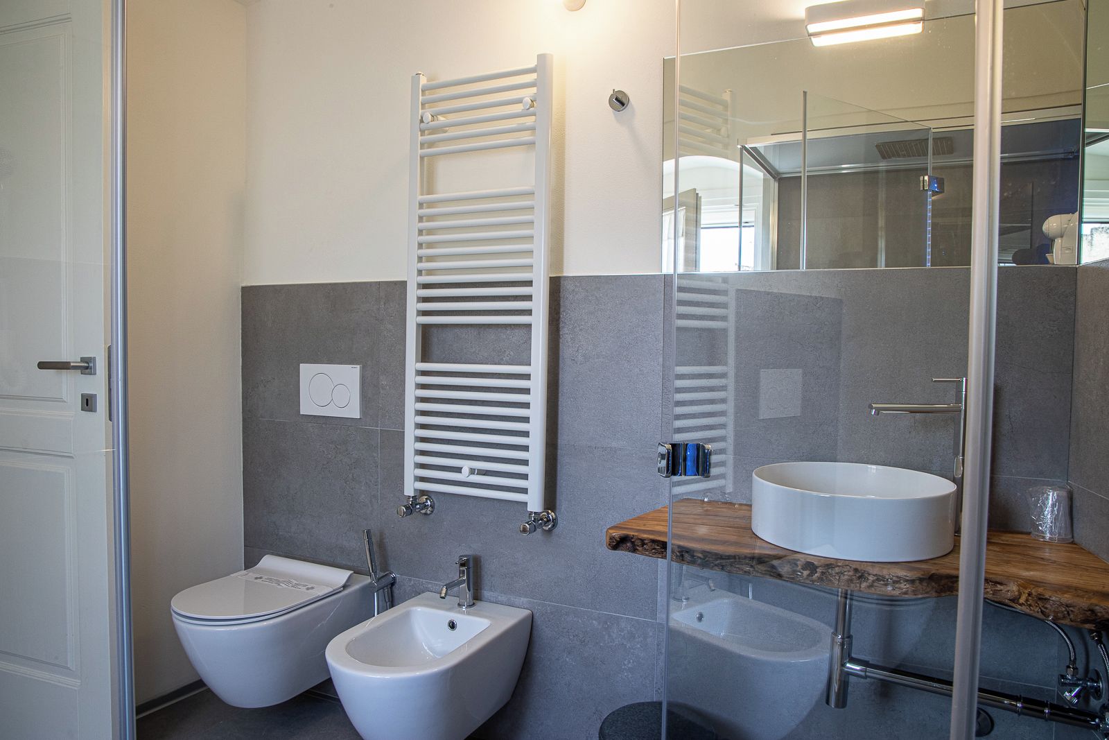 Ein modernes Badezimmer mit zwei Bidets, einem weißen Waschbecken und einer Duschkabine aus Glas.