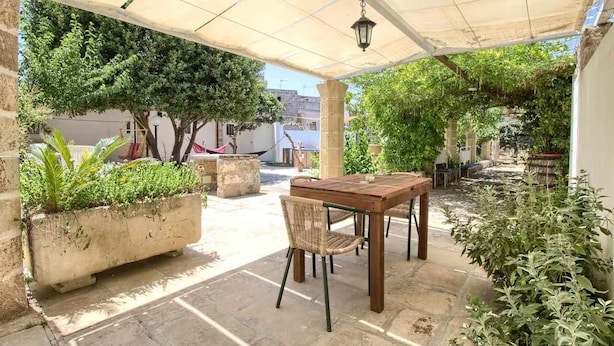 An outdoor patio with a table and chairs, surrounded by potted plants and trees. - La Cantina - BB La Traja (Gagliano del Capo)