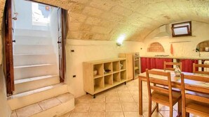 A kitchen with a tiled floor, wooden cabinets, a dining table with chairs, and a window with a view of the outside. - La Cantina - BB La Traja (Gagliano del Capo)