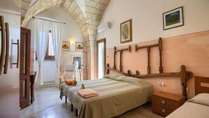 A bedroom with a large bed, a smaller bed, a wooden headboard, a nightstand, a chair, and a window with curtains. - La Cantina - BB La Traja (Gagliano del Capo)