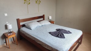 A neatly made bed with a patterned bedspread, two pillows, a wooden headboard, two bedside tables with lamps, and a towel on the bed. - Full equipped bungalows with swimming pool, wifi, garden for 2 to 5 people (Morro)