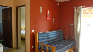 A room with a wooden sofa against a red wall, a door leading to another room, and a small table with a chair. - Full equipped bungalows with swimming pool, wifi, garden for 2 to 5 people (Morro)