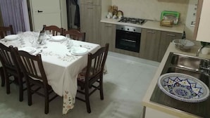 Un coin repas avec une table dressée pour six personnes, une cuisine équipée d’une cuisinière et d’un four, et un évier agrémenté d’un dosseret décoratif en carreaux.