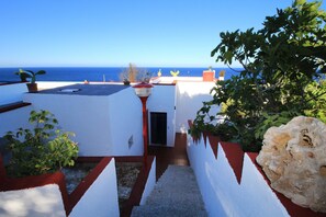 Une terrasse sur le toit offrant une vue sur la mer, agrémentée de plantes en pot et ornée d’un motif mural rouge et blanc.