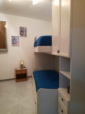 Une chambre avec des lits superposés, une table de chevet et une commode.
