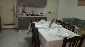 Un coin repas avec une table dressée pour six personnes, une cuisine en arrière-plan et une porte donnant sur une autre pièce.