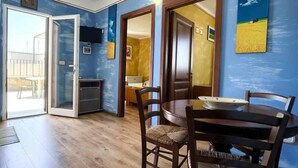 A dining area with a round table and chairs, a sliding glass door leading to a balcony, and a kitchen area visible through the door. - Terrazza 1 - BB La Traja (Gagliano del Capo)