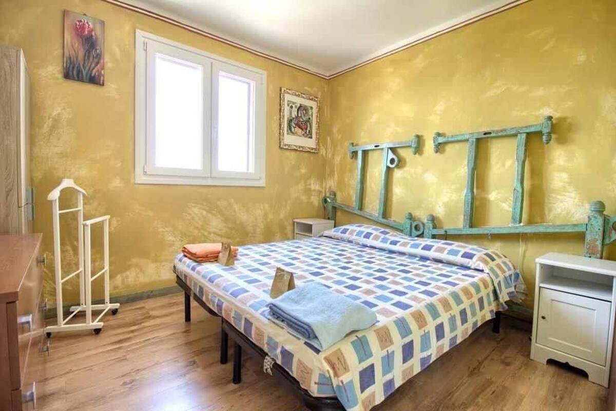 A bedroom with a bed, a nightstand, a dresser, a window, and a wall-mounted rack.