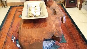 A room with a wooden table holding a tray of eggs, a small wooden cabinet, and a patterned rug. - Machakos Luxury Suites (Machakos)