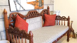 A wooden sofa with a woven seat and backrest, two red cushions, and a decorative metal plate on the wall behind. - Machakos Luxury Suites (Machakos)