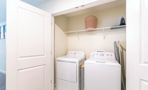 A laundry room with two stacked washers and dryers, a shelf with a basket, and a hanging rack. - South-Facing Pool & Spa • Princess Room • Game Room • Near Disney (Davenport)