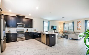 A modern kitchen with dark cabinetry, stainless appliances, and a marble floor.