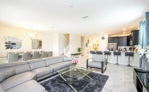 A modern living room with a sectional sofa, a glass coffee table, and a dining area with chairs.
