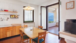 Una cocina con armarios de madera, una mesa de comedor con sillas, una lámpara colgante y vistas a un balcón exterior a través de una puerta abierta.