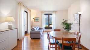 Una sala de estar moderna con sofá, mesa de comedor, sillas y vista al mar a través de amplios ventanales.