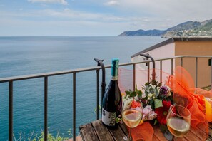 Un balcon avec vue sur la mer, une bouteille de vin et un bouquet de fleurs.