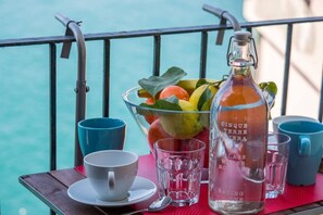 A table with a glass bottle, a bowl of fruit, and two cups on a balcony with a view of the sea. - Il Baluardo Sea View Apartment on the Cliff (Manarola)