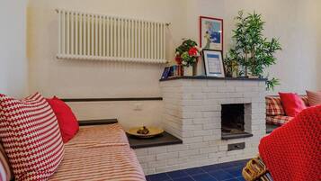A living room with a white brick fireplace, a radiator, and a sofa with red cushions.