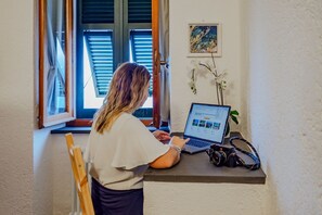 Iemand werkt aan een bureau bij een raam met jaloezieën, een laptop en een camera op tafel.