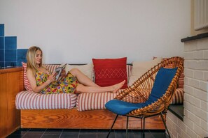 A person sitting on a sofa with striped cushions, a red pillow, and a blue chair with a woven backrest.