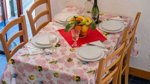Une table à manger dressée avec des assiettes, des couverts, un verre, une serviette rouge, un saladier de fruits et une bouteille d’eau.