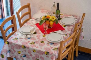 Une table à manger dressée avec des assiettes, des couverts, un verre, une serviette rouge, un saladier de fruits et une bouteille d’eau.