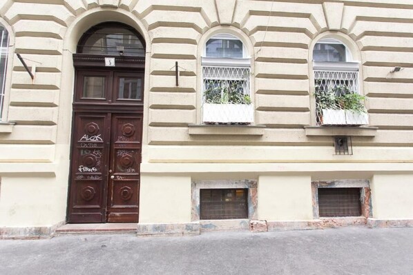 A building with a large arched entrance door, two windows with white railings, and a small window with a metal grate.