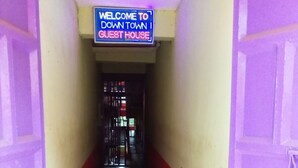 Un pasillo con suelo de mosaico que conduce a una puerta, un letrero que dice 'Welcome to Down Town Guest House' y una reja al final.
