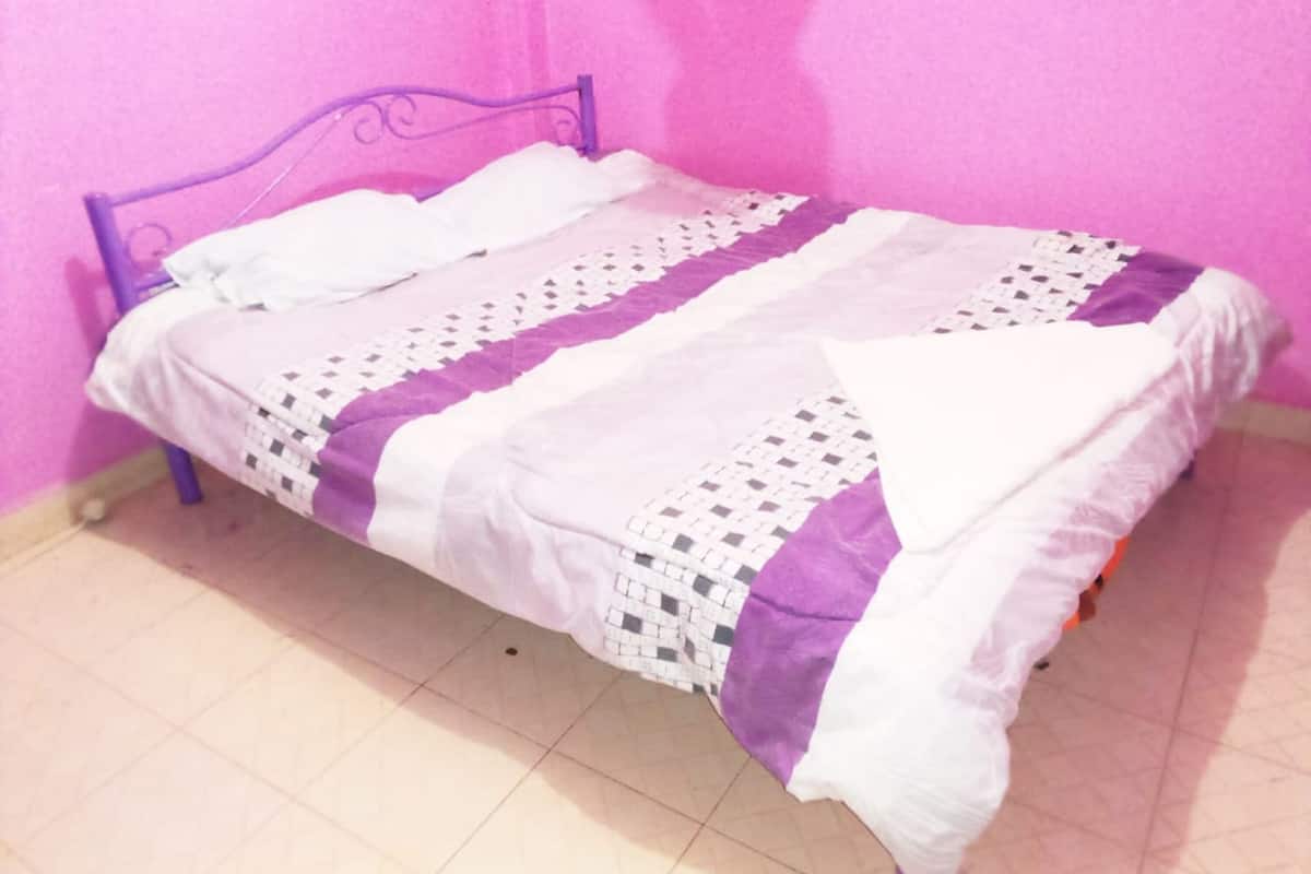 Una cama con estructura metálica morada, ropa de cama blanca y morada, y una manta estampada.