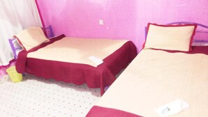 Dos camas individuales con ropa de cama roja y color beige, un cesto de basura amarillo pequeño y una cortina blanca.