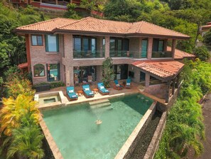 A two-story house with a swimming pool, surrounded by lush greenery.