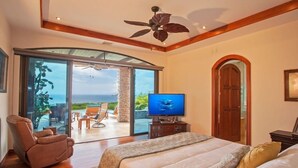 A bedroom with a large bed, a television, and a view of the ocean through a sliding glass door. - Casa de los Suenos (Sardinal)