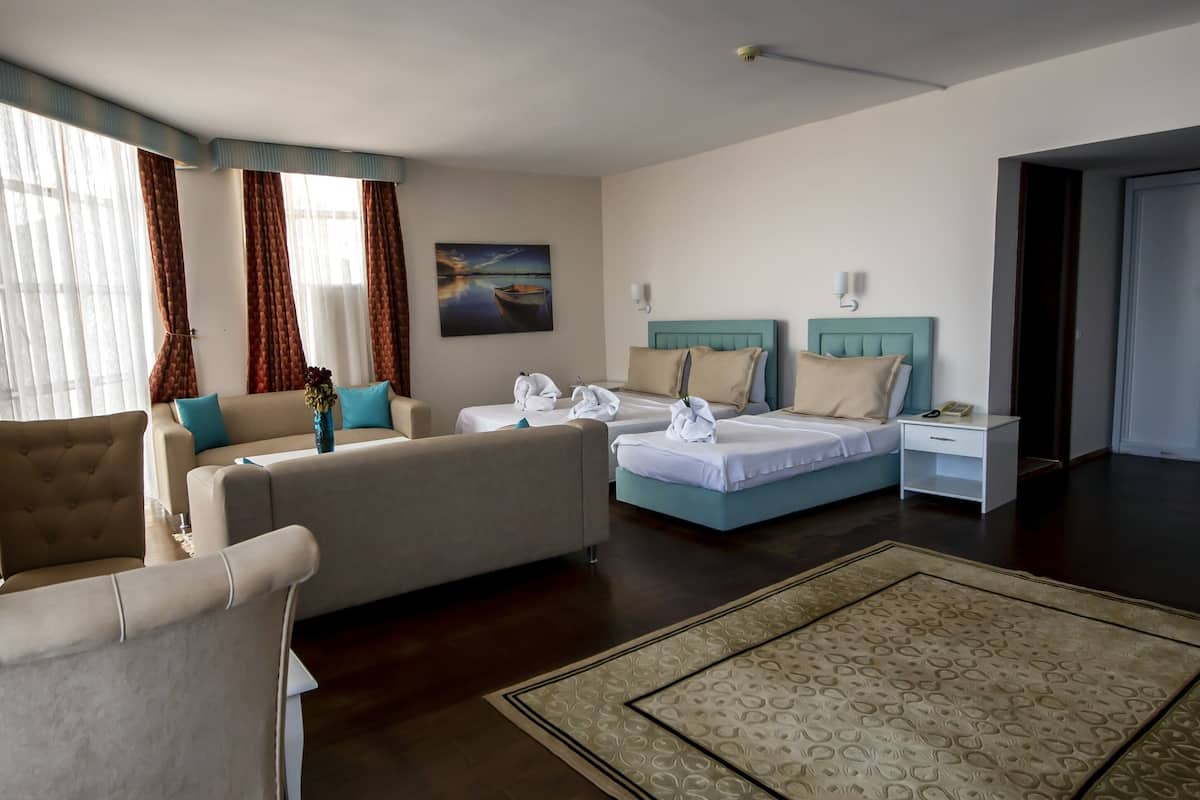 Una habitación de hotel con sofá, cama, mesita de noche y un ventanal con cortinas.